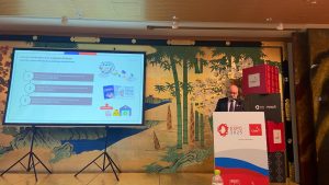 Jorge Daza, Subsecretario de Transportes de Chile, expone sobre logística urbana y transformación digital en el Seminario de Servicios Públicos durante la Semana de la Logística en Expo Osaka. La imagen muestra a Daza frente a una audiencia, discutiendo avances en infraestructura portuaria y transporte ferroviario de carga.