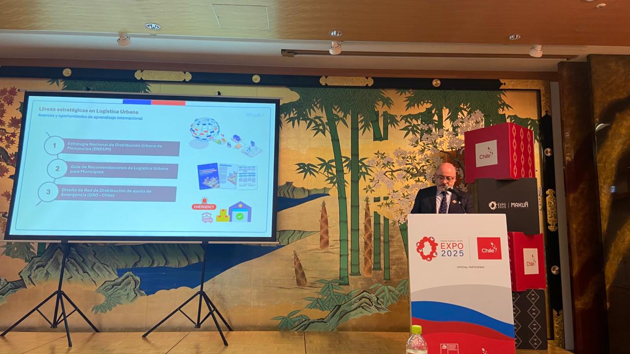 Jorge Daza, Subsecretario de Transportes de Chile, expone sobre logística urbana y transformación digital en el Seminario de Servicios Públicos durante la Semana de la Logística en Expo Osaka. La imagen muestra a Daza frente a una audiencia, discutiendo avances en infraestructura portuaria y transporte ferroviario de carga.